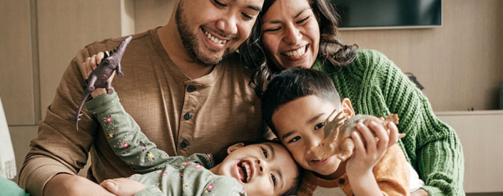 A mother and father laugh while their two children play with dinosaur toys.