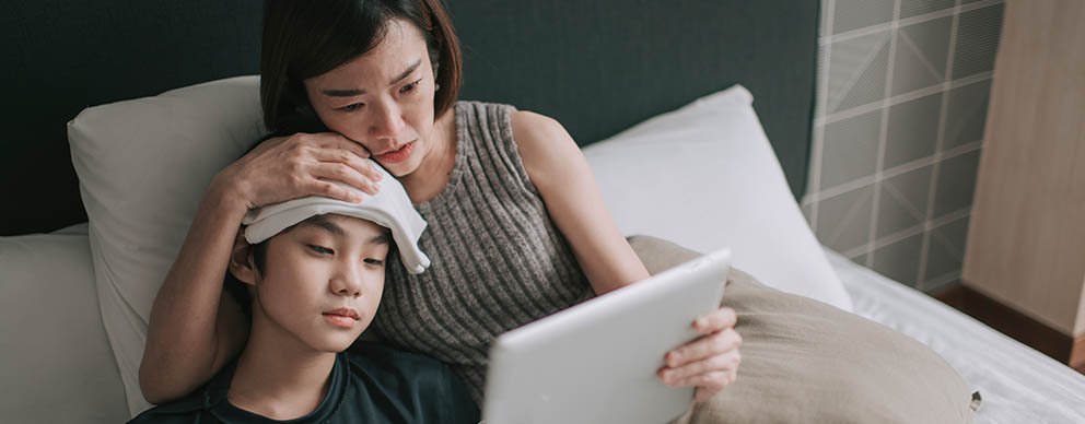 A mother holds a tablet up for her son who is sick.